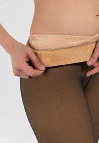 Czarne, przezroczyste rajstopy z miękkim, beżowym pasem z materiału pluszowego, które są regulowane ręką, charakteryzujące się eleganckim designem i gładką teksturą.