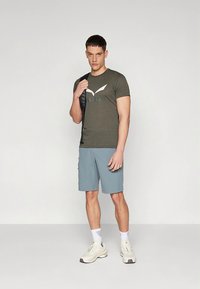 Meeste spordiriietus, mis koosneb oliivrohelisest t-särgist valge logoga ja helesinistest lühikestest pükstest. Komplektsioon sisaldab valgeid tossusid ja musta seljakotti.