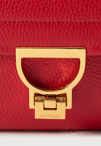 Borsa a mano in pelle rossa con texture, caratterizzata da una fibbia metallica dorata con manico ovale e dettaglio del logo inciso alla base.