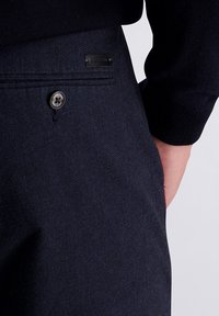 Donkerblauwe broek van gestructureerde stof, voorzien van een knoopsluiting en een merklabel op het zakje, met een getailleerde pasvorm.