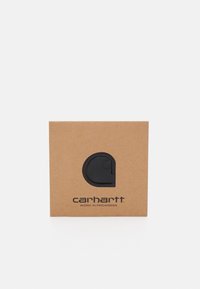 Brun papkasse med et sort cirkulært logo og tekst "carhartt" sammen med "WORK IN PROGRESS" i sort skrift under logoet.