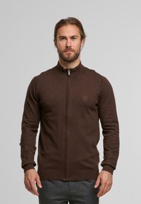 Brauner Zip-up-Pullover mit hohem Kragen, gerippten Bündchen und einem dezenten Logo auf der Brust. Glatte Textur und figurbetontes Design.