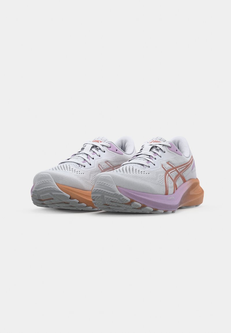 Baskets de sport blanches avec des accents violets et orange, présentant une tige en maille texturée, un système de laçage et une semelle en caoutchouc contrastante.