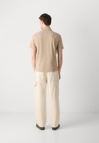 Polo en coton beige associé à un pantalon crème ample avec des poches latérales. Design simple, manches courtes et coupe décontractée.