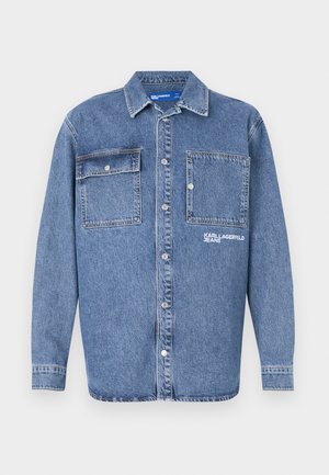 Chaqueta de mezclilla azul claro con un cuello clásico, dos bolsillos en el pecho con botón y el logo bordado "KARL JEAN". Cierre de botones en la parte delantera.