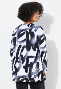 Maglietta a maniche lunghe in bianco e nero con motivo astratto, realizzata in tessuto morbido con vestibilità rilassata, colletto rotondo e orlo curvo.