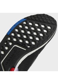 Black sneaker outsole featuring a hexagonal pattern, blue and red accents, textured rubber, and a cushioned white midsole.