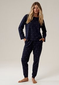 Granatowy komplet piżamowy z miękkiego materiału, z długimi rękawami i elastycznym pasem. Udekorowany małymi, okrągłymi różowymi wzorami w całym zestawie.