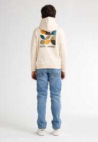 Felpa beige con un design grafico in verde, giallo, blu e marrone. Abbinata a jeans azzurri chiari e sneaker bianche.