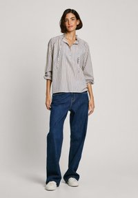 Stripet bomulds skjorte med standkrave og knaplukning, parret med løse mørkeblå denimjeans og hvide sneakers.