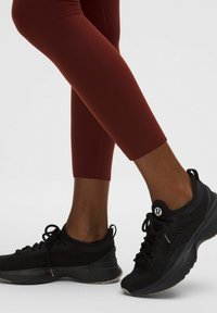 Fekete sportcipők hálós panelekkel, lapos fűzővel és párnázott talppal, amelyekhez szoros, bordó, bokáig érő leggings párosul.