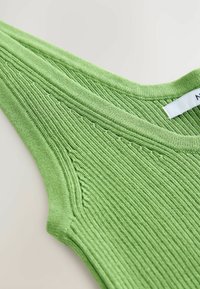 Haut tricoté vert avec une texture côtelée, un large décolleté et des épaules légèrement effilées. L'étiquette affiche le nom de la marque sur une étiquette blanche.