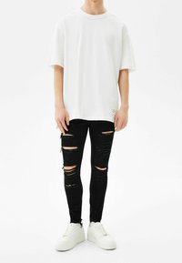 Vit oversized t-shirt med rund hals, kombinerad med svarta slitna skinny jeans med hål. Bärs med vita sneakers.