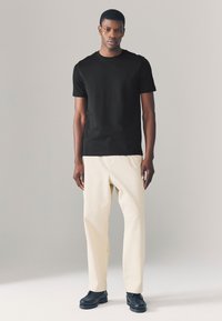 Black short-sleeve t-shirt, beige wide-leg trousers, black shoes, standing on a neutral background. Simple, modern design with smooth fabric.