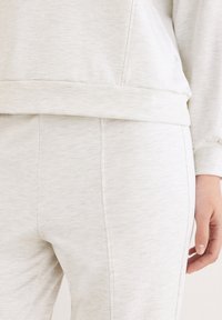 Lichtgrijze loungewear-set met een sweatshirt met een geribbelde zoom en een broek met zijnaad. De stof lijkt zacht en lichtjes gestructureerd.