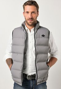 Graue, gepolsterte Weste mit hohem Kragen, schwarzen Akzenten, Frontreißverschluss und zwei Seitentaschen, getragen über einem weißen Hemd und blauen Jeans.