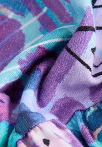 Soft fabric with a colorful abstract pattern in shades of purple, blue, and black, shown in a close-up with folds and texture details.
