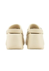 Zuecos beige con un acabado suave y brillante. Cuentan con una amplia correa trasera curvada y un diseño de punta redondeada. Suela ligera y antideslizante.