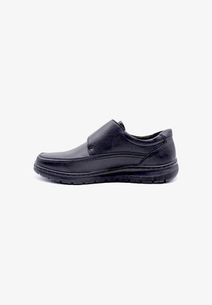 Chaussure slip-on en cuir noir avec une surface lisse, bout arrondi et semelle texturée pour une meilleure adhérence. Design minimaliste sans quincaillerie visible.