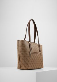 Brązowa torba tote o teksturowanym wykończeniu, z subtelnym wzorem logo, podwójnymi brązowymi uchwytami oraz przednią kieszenią na zamek.