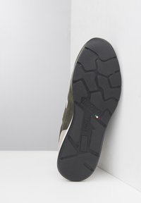 Scarpa sportiva leggera di colore verde oliva con una suola in gomma nera testurizzata. Presenta un accento bianco e dettagli di branding in rilievo.