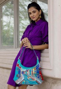 Een turquoise handtas met een levendig geschilderd tafereel van kleurrijke gebouwen en een kanaal, voorzien van een schouderband en decoratieve accenten.