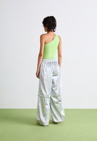 Débardeur asymétrique vert associé à un pantalon large en argent réfléchissant. Le matériau semble brillant avec une taille élastique et des détails froncés.