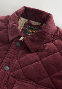 Bordeaux corduroy jack met een geborgte ontwerp, een zachte crèmekleurige voering en zwarte drukknoopknopen op de kraag en de voorzakken.