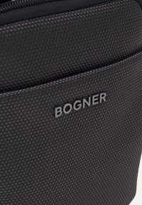 Sort tekstureret stoftaske med et forhøjet BOGNER-logo. Glat lynlåslukning og en struktureret design for holdbarhed og funktionalitet.