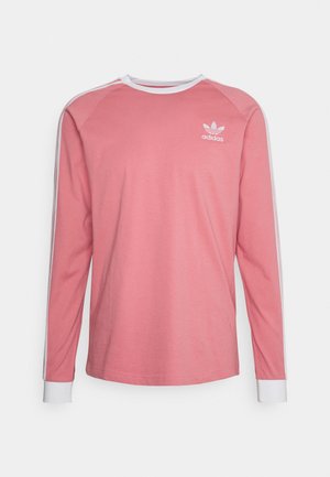 Chemise Adidas rose à manches longues avec poignets, col et bandes sur les manches blancs, arborant le logo trèfle Adidas sur la poitrine.