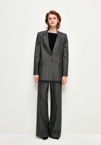 Completo grigio scintillante composto da blazer e pantaloni a gamba larga, caratterizzato da un tessuto testurizzato, due tasche frontali sul blazer e una chiusura con un solo bottone.