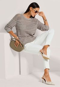 Grauer Strickpullover mit offener Webart, weiße eng anliegende Hosen, beigefarbene Slingback-Absätze, olivgrüne Handtasche, übergroße Sonnenbrille, strukturierte Accessoires.