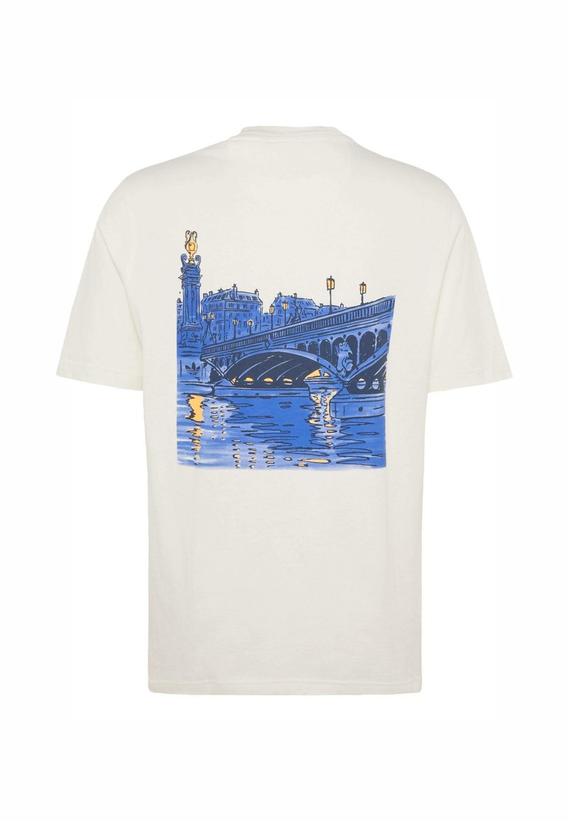 T-shirt beige avec graphisme bleu et jaune d'un pont de ville au-dessus de l'eau au crépuscule dans le dos.