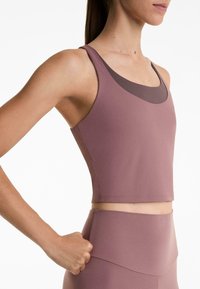 Ljubičasti atletski crop top s okruglim izrezom i tankim trakama. Izrađen od glatkog, rastezljivog materijala, ima slojeviti dizajn na izrezu.