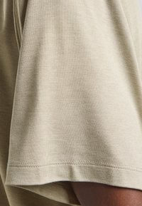 Helles beige Baumwoll-T-Shirt mit kurzen Ärmeln, weicher Textur und sauberem Abschluss. Minimalistisches Design, das keine Muster oder Akzente aufweist.