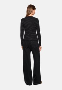 Black ribbed sweater with a subtle zebra pattern, paired with loose-fitting black jeans. The sweater has long sleeves and a round neckline.