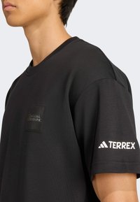 Black T-shirt featuring a textured National Geographic logo patch on the chest and a white Adidas Terrex logo on the sleeve.