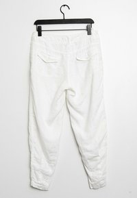 Vita linbyxor som hängs på en svart galge. Funktioner inkluderar en lös passform, bakfickor och en subtil textur.