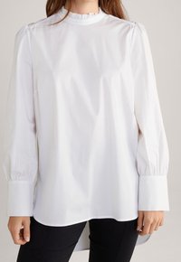 Blusa bianca a maniche lunghe in tessuto leggero, con un collo alto arricciato, cuciture delle spalle gathered e ampi polsini.