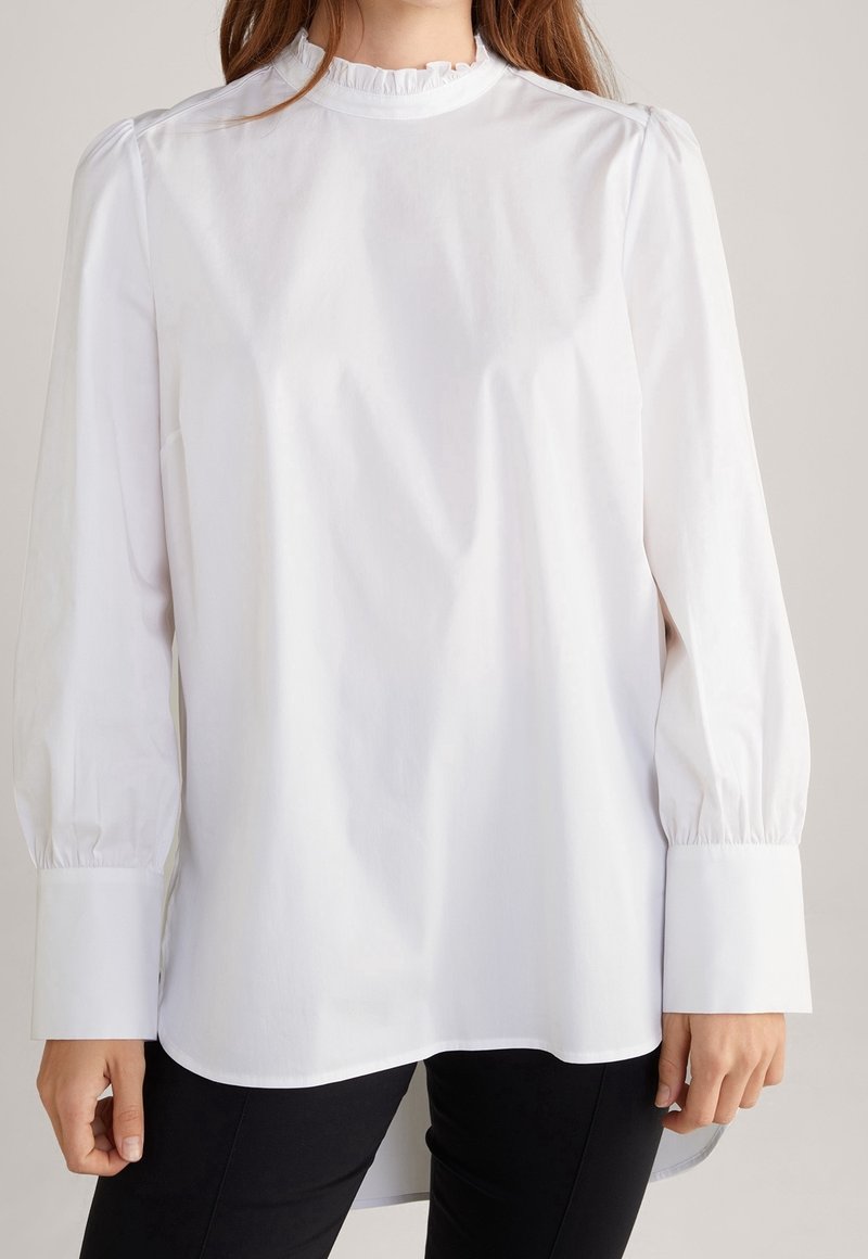 Blusa bianca a maniche lunghe in tessuto leggero, con un collo alto arricciato, cuciture delle spalle gathered e ampi polsini.