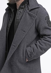 Płaszcz typu peacoat z mieszanki wełny, ciemnoszary, z podwójnym zapięciem na guziki, dużymi guzikami oraz czarną pikowaną podszewką wewnętrzną z kołnierzem stójką.