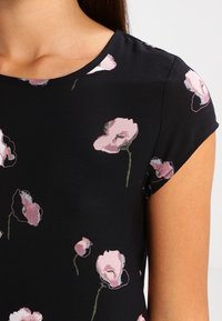 Černé tričko s krátkým rukávem, které má růžové květinové vzory. Materiál vypadá měkce s hladkou texturou a kulatým výstřihem.