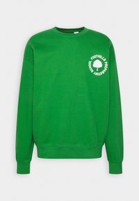 Sudadera verde con cuello redondo, mangas largas y texto blanco junto a un logo de árbol en el lado izquierdo del pecho. Textura suave y diseño de corte relajado.