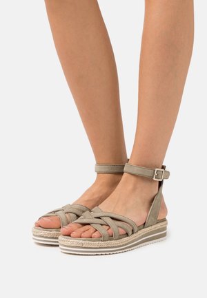 Sandalias de tiras beige con diseño trenzado, hebilla en el tobillo y suela estilo esparto que presenta un acento de cuerda texturizada y una base de goma.