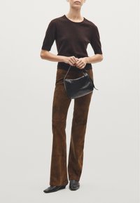 Dark brown short-sleeve knit top, paired with brown suede flared pants. A small black leather handbag is held in the front; pointed black shoes worn.