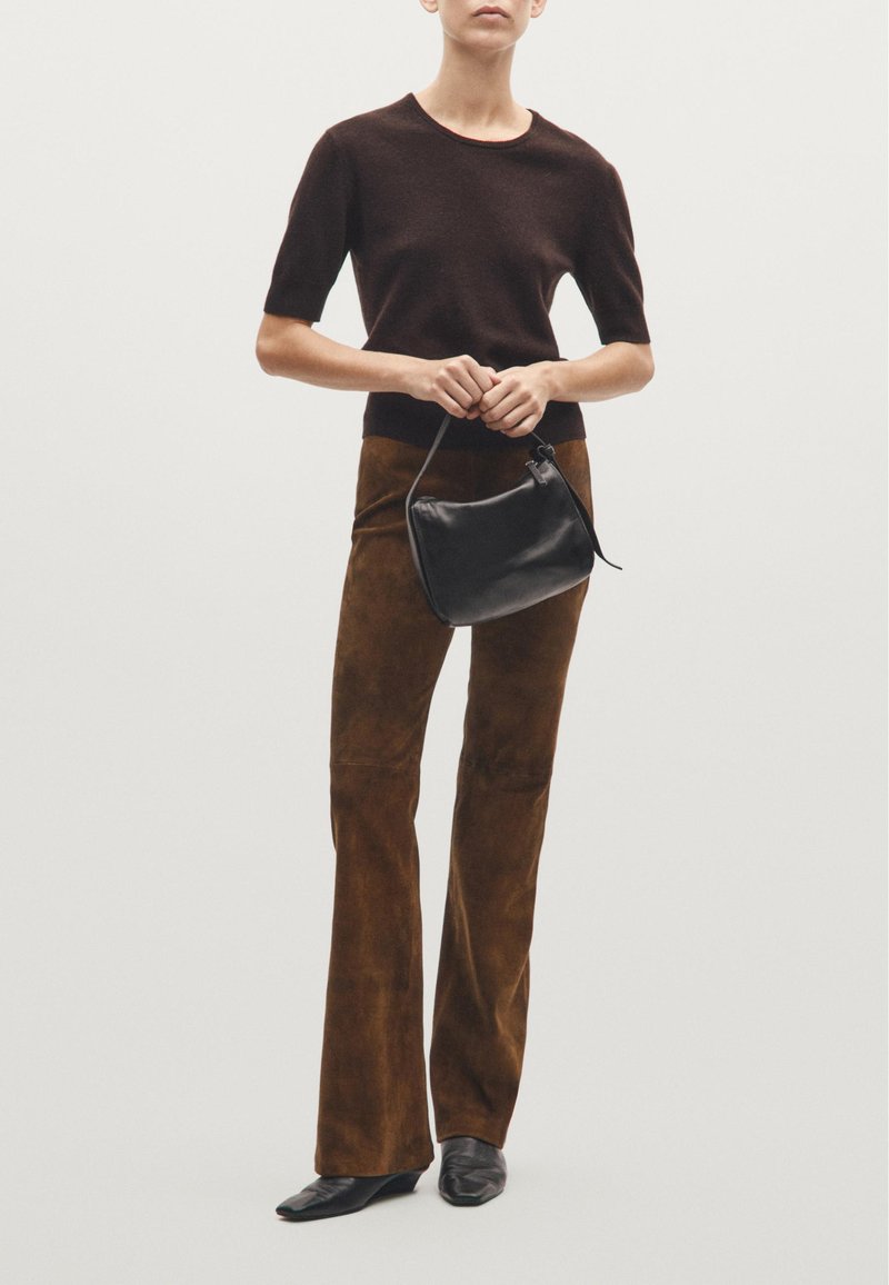 Dark brown short-sleeve knit top, paired with brown suede flared pants. A small black leather handbag is held in the front; pointed black shoes worn.