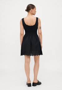 Μαύρο αμάνικο φόρεμα με σμπαρωμένη μέση, διακοσμημένο με δαντελένια περιθώρια σε κυματιστό σχέδιο. Λείο υφάσμα με χαμηλή πλάτη και απλό σχέδιο.