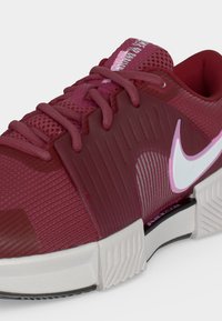 Κοντινή λήψη μπορντό αθλητικού παπουτσιού Nike με ροζ λεπτομέρειες, υφαντό επάνω μέρος με υφή, επενδυμένη σόλα και λεπτομερή κορδόνια.