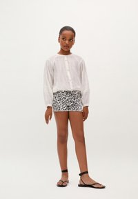 Camisa blanca de manga larga con cierre de botones y sutiles rayas texturizadas, combinada con unos shorts de estampado de leopardo. Sandalias planas negras con tiras.