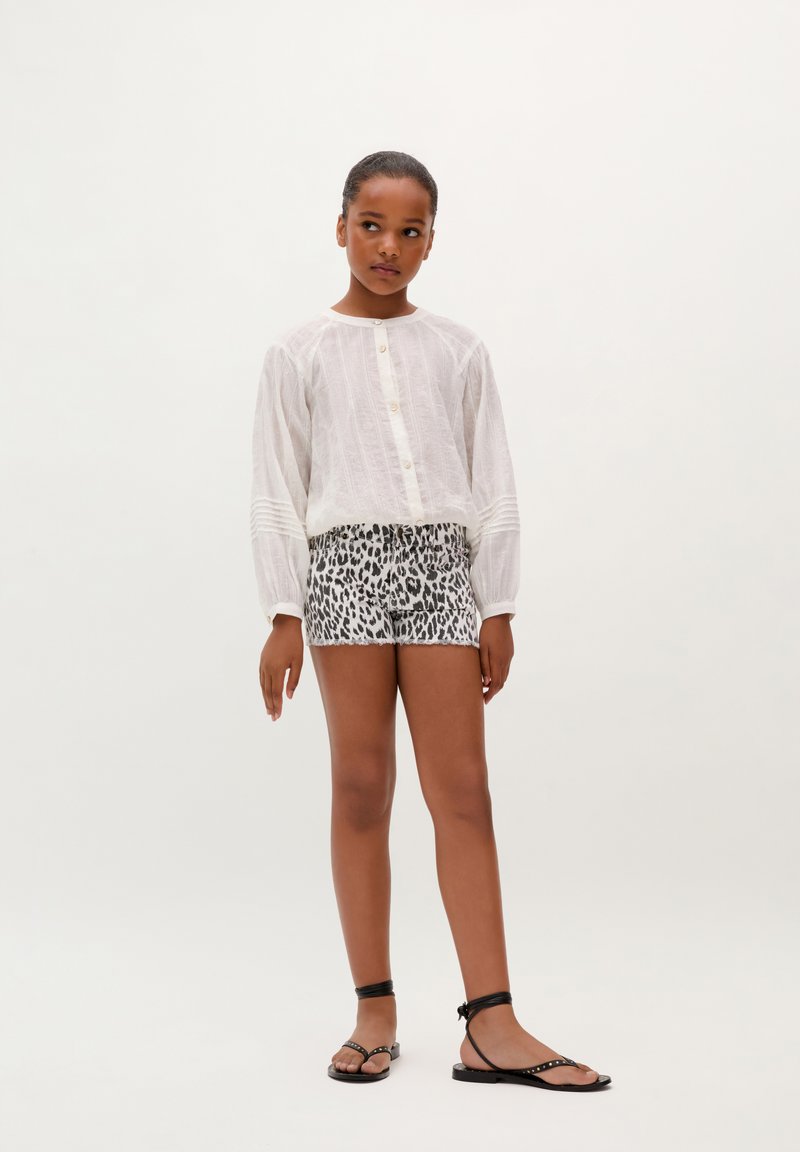 Camisa blanca de manga larga con cierre de botones y sutiles rayas texturizadas, combinada con unos shorts de estampado de leopardo. Sandalias planas negras con tiras.